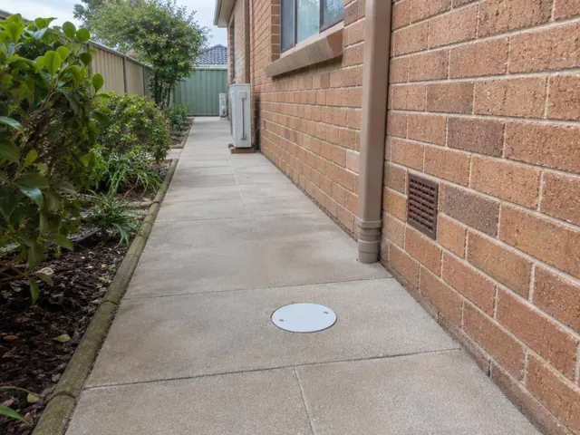 Covered outdoor drain beside a brick house and paved side path in St Ives