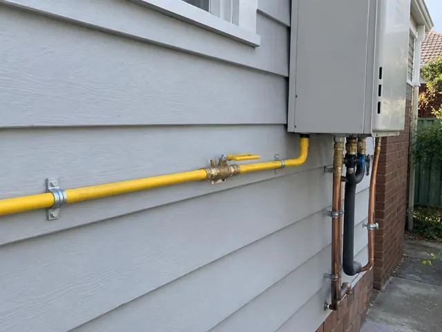 Yellow gas pipe and fittings on a house exterior beside a wall-mounted unit in Gordon
