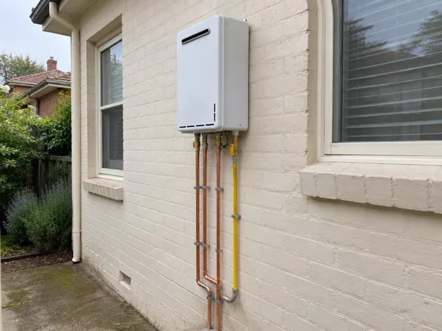 Wall-mounted hot water unit with copper and gas pipes on a painted brick exterior wall in Roseville
